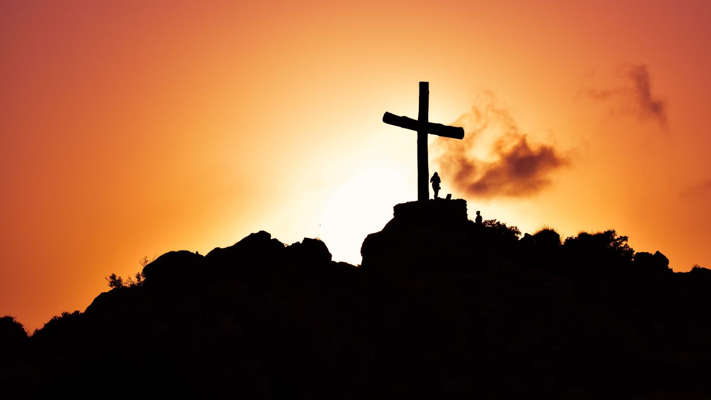 A cross on a hilltop silhouetted against the sunrise