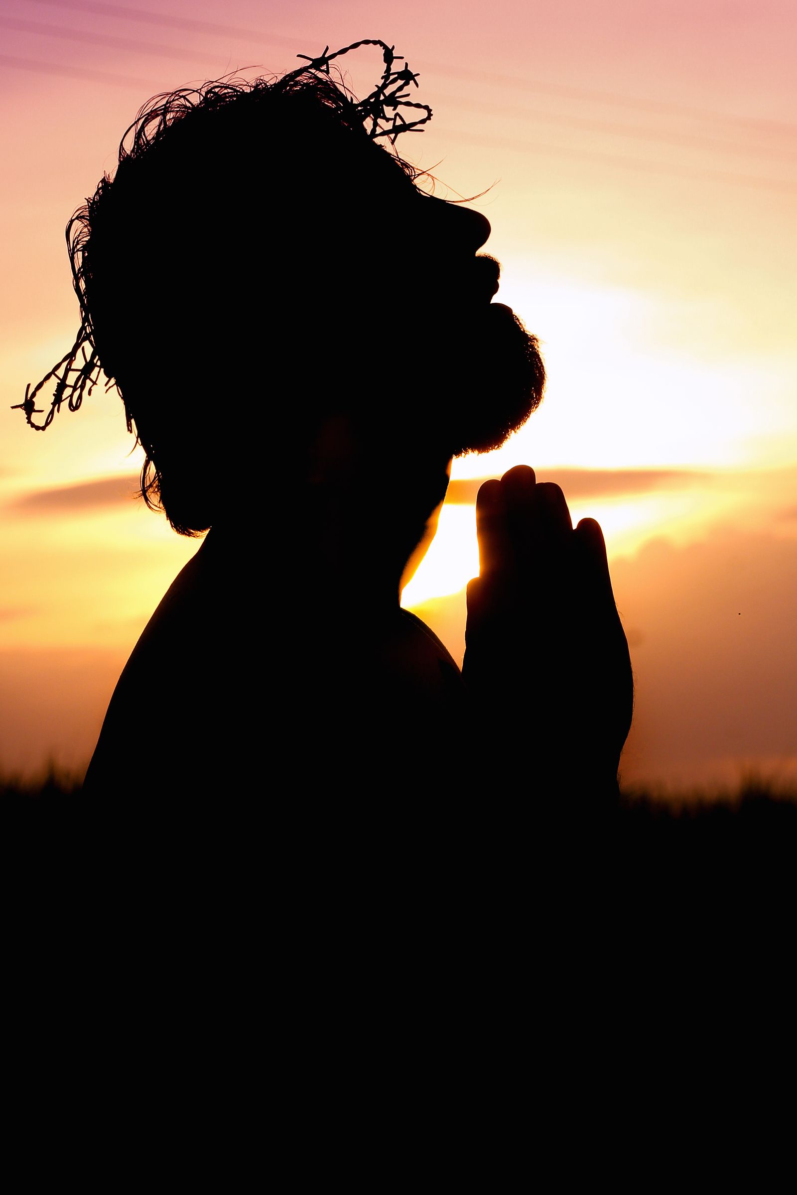 A person praying outdoors as the sun rises