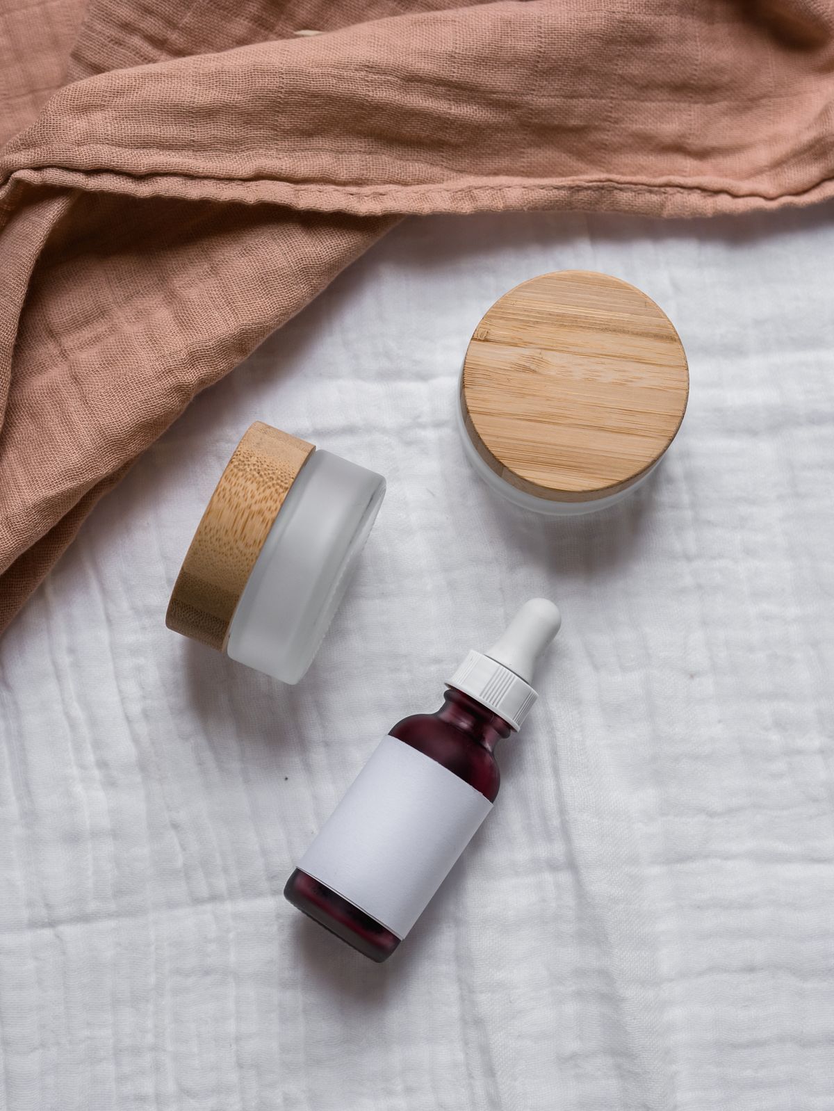 Natural skincare jars and a dropper bottle on soft fabric